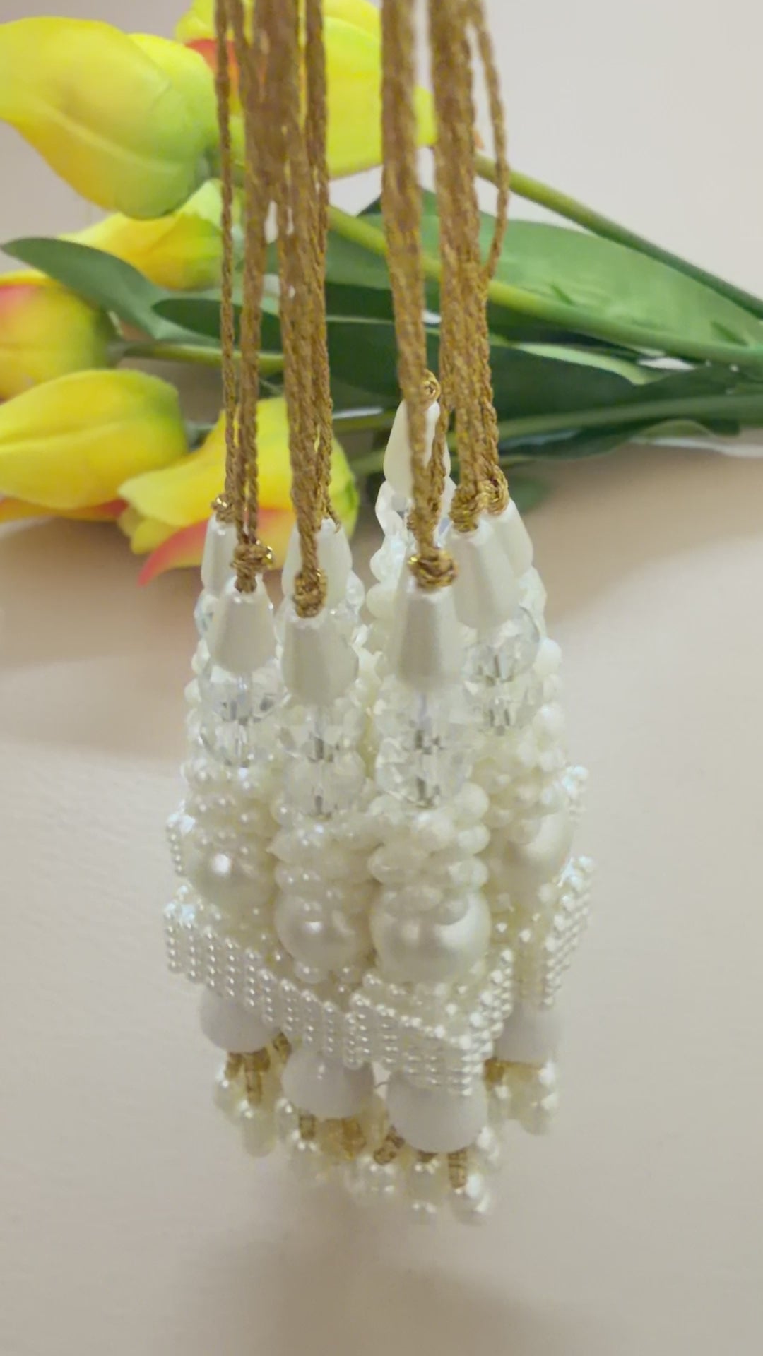 Pearl and gold decorative item held in a hand with yellow flowers in the background