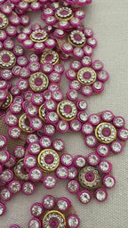 Decorative button with pink and gold accents next to a ruler on a textured surface