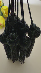 Black tassel held in a hand against a beige background