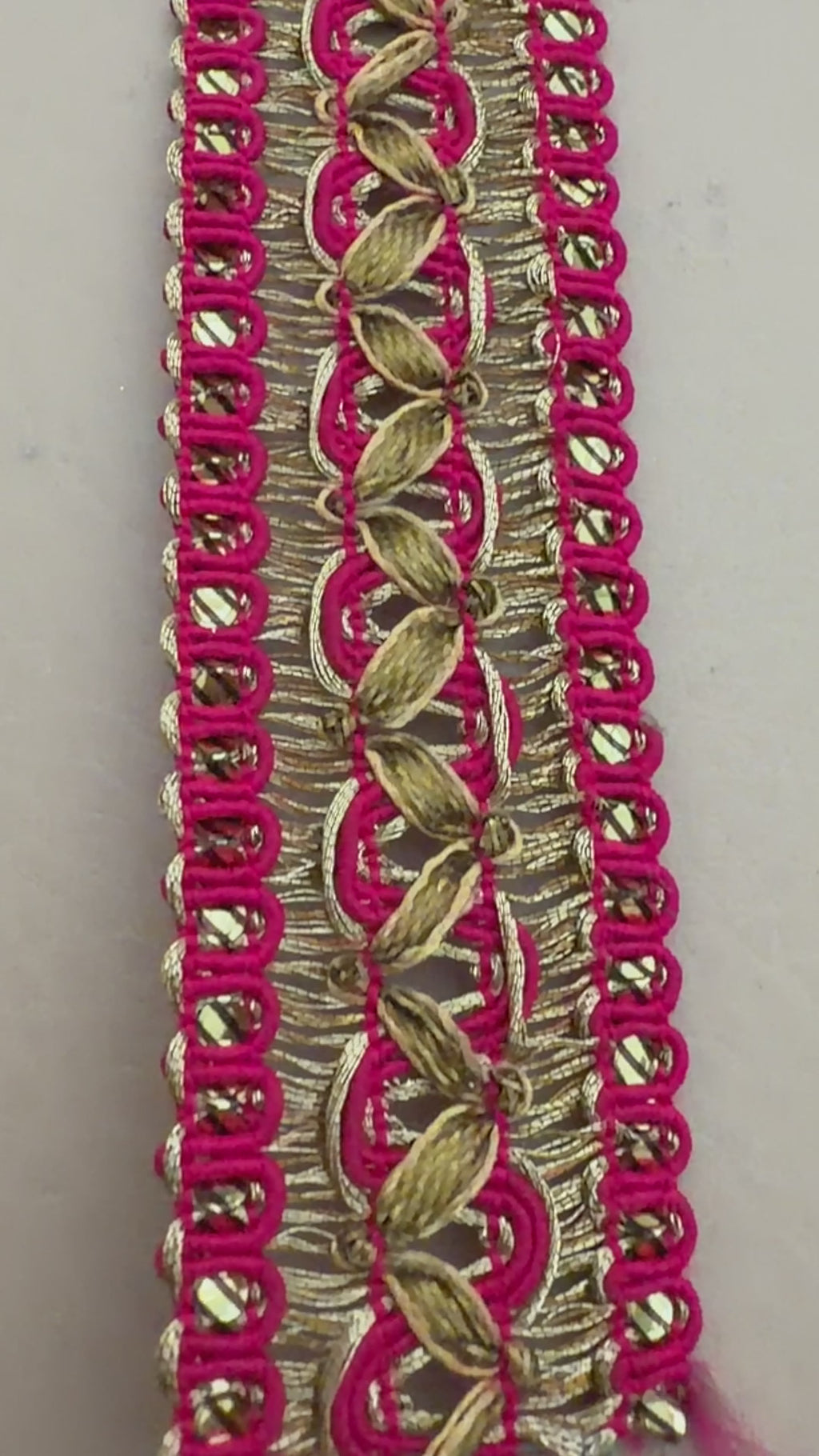 Roll of pink ribbon with gold lace trim next to a white flower on a beige background