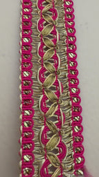 Roll of pink ribbon with gold lace trim next to a white flower on a beige background
