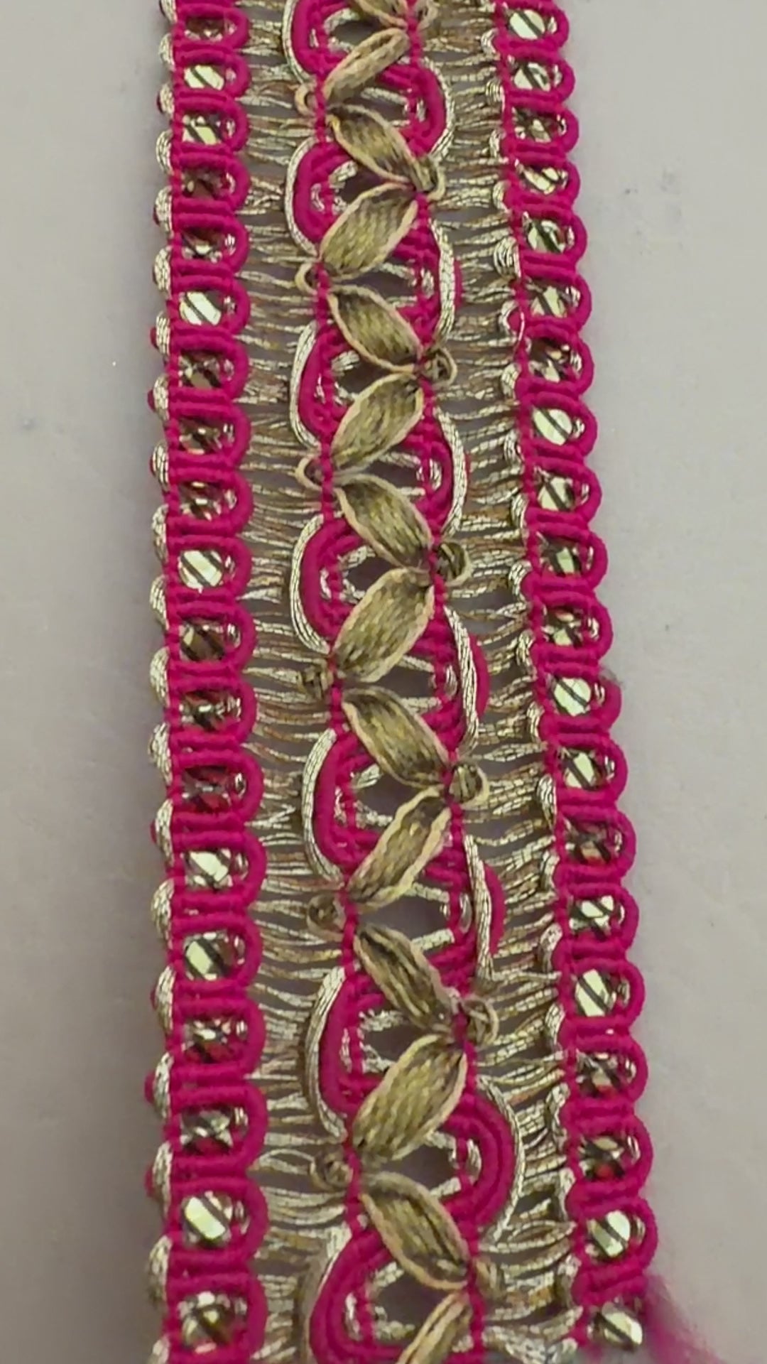 Roll of pink ribbon with gold lace trim next to a white flower on a beige background