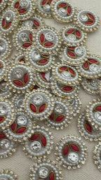 Close-up of decorative buttons with red centers, pearls, and crystals on a beige background