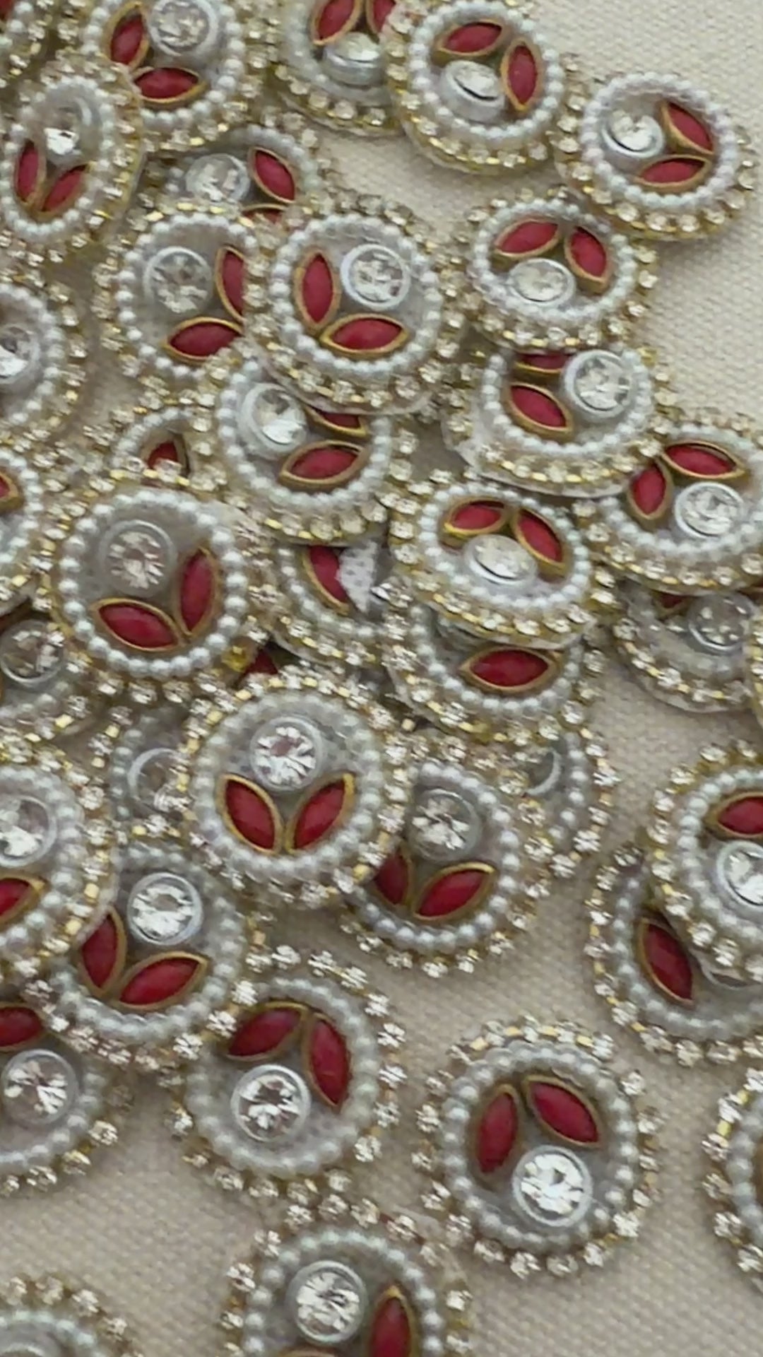Close-up of decorative buttons with red centers, pearls, and crystals on a beige background
