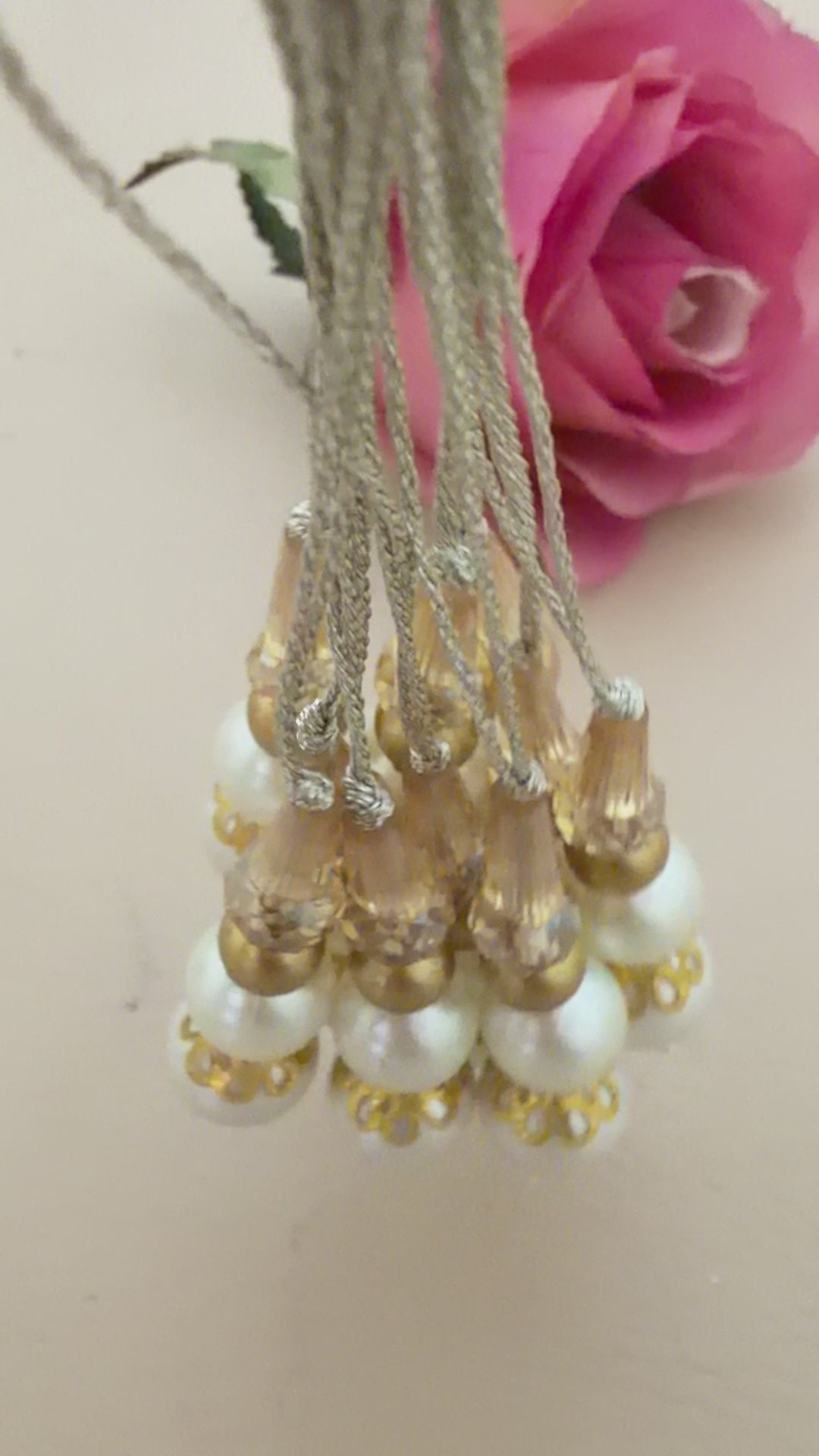 Set of pearl and gold beaded hair accessories with a pink rose on a beige background