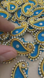 Decorative paisley patch with blue center and gold border next to a ruler for scale.