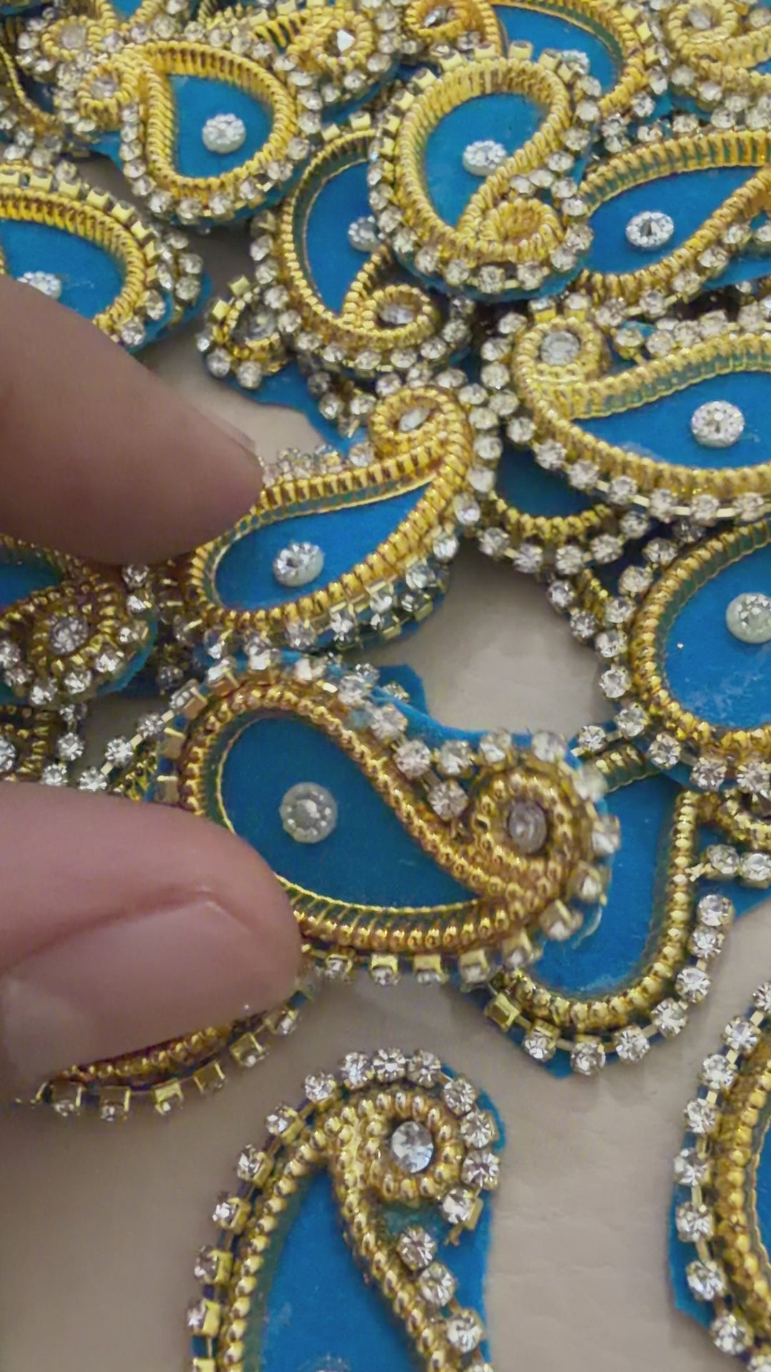 Decorative paisley patch with blue center and gold border next to a ruler for scale.
