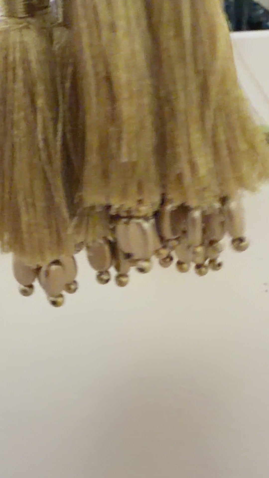 Gold tassels with beads on a light gray background